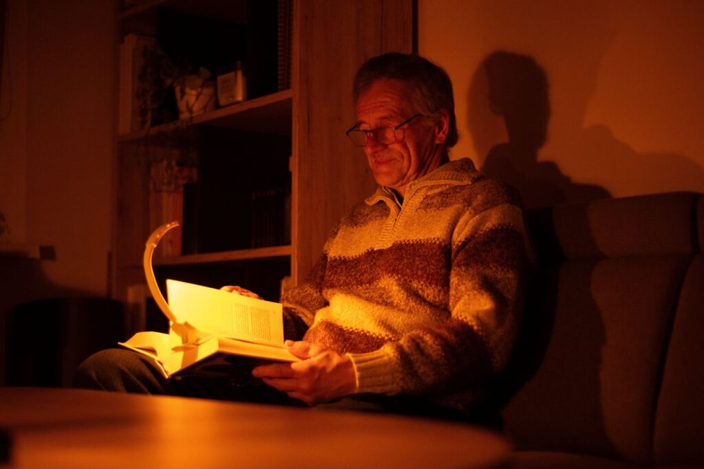 Starší muž si čte knížku a svítí si večerní LED lampičkou ORANŽOVKA